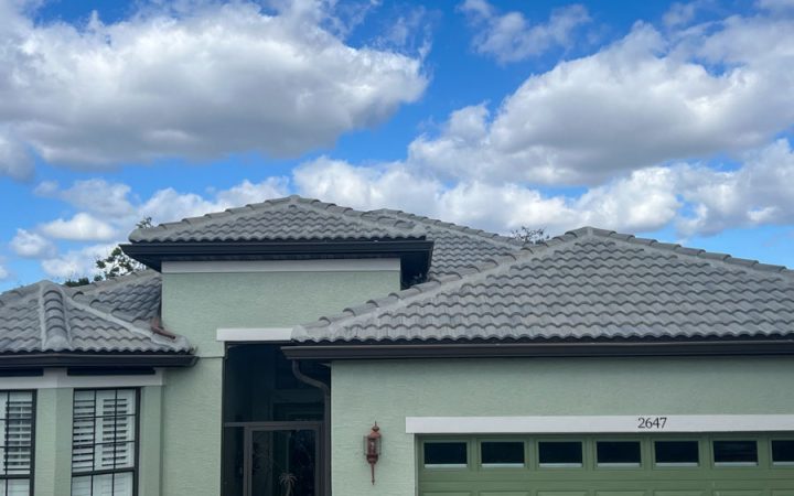 View of a residential roof with grey clay tiles against a partly cloudy sky, emphasizing the robust design of modern roofing materials.