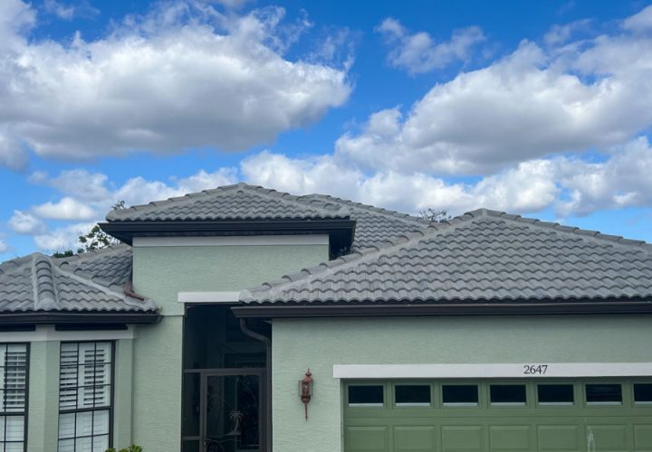 View of a residential roof with grey clay tiles against a partly cloudy sky, emphasizing the robust design of modern roofing materials.